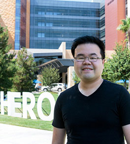 Michael Nguyen, wearing a black t-shirt, stands in front of UCI Medical Center and the "Heroes work here" sign.