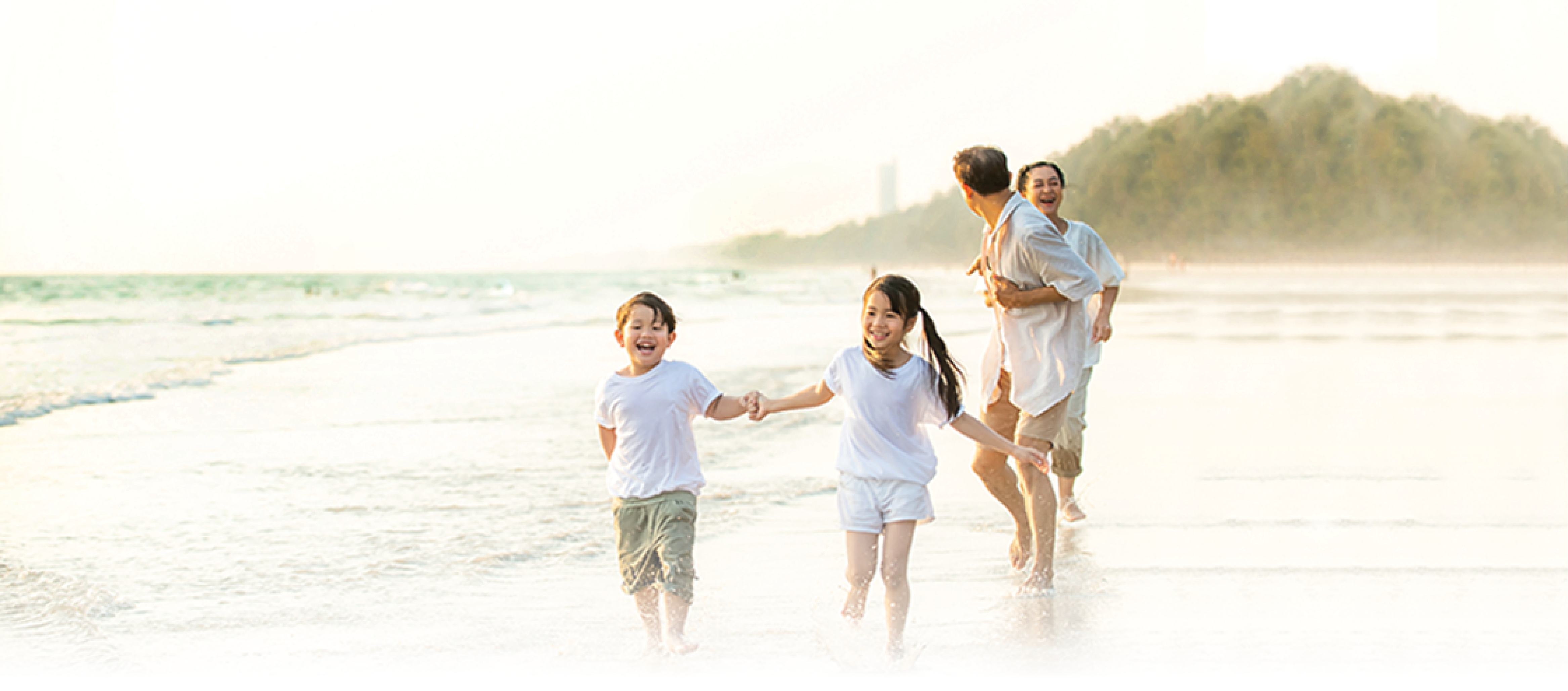 Family of four plays at the beach with coastline in background
