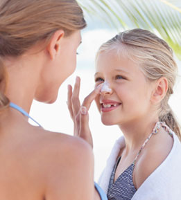 Young mother applies sunscreen to her daughter's nose.