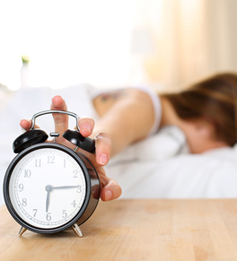 woman hitting snooze on alarm clock 