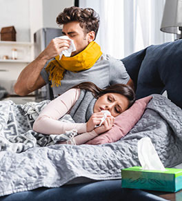 Young couple laying in bed, suffering from flu symptoms.