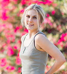 Kayden Lincoln in gray tank top stands in front of pink bouganvillea. 