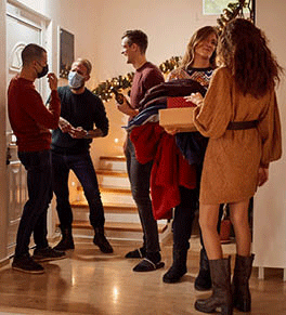 A group of adults, some wearing masks, gathered in a foyer at the holidays..