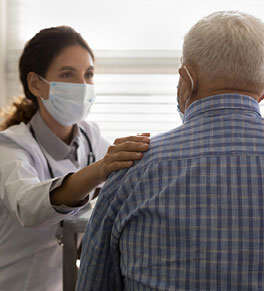 Empathic young female doctor in medical mask puts her hand on shoulder of elderly man patient.