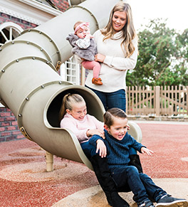 Tatum Miller and baby Evie, six months, look on as sister Payton, 10, and brother Easton, 3, tumble from a park slide.