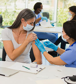 Middle aged woman watches as a nurse gives her a booster shot.