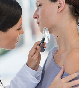 A female doctor uses a magnifier to check a mole on a female patient's neck.