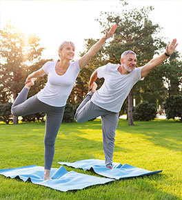 A senior couple practices yoga in a beautiful park.