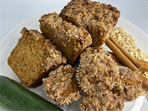 Zucchini coffee cake and muffins displayed with oats and cinnamon sticks.