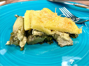 Baked artichoke and spinach polenta in a blue dish.