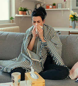 Woman suffering from the flu stays warm with a striped blanket while blowing her nose.