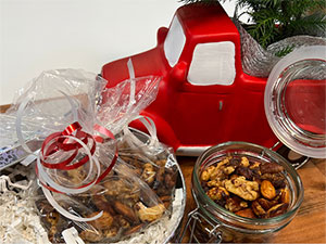 Open jar of spiced and candied nuts in by a gift box in front of a red truck.