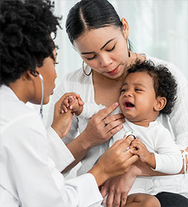 A crying toddler sitting on his mother's lap gets a checkup from a pediatrician.