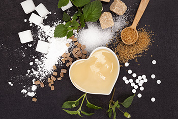 Multiple sugar substitutes are displayed on a black background with a heart-shaped bowl of honey.