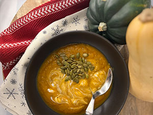 Butternut squash soup garnished with pumpkin seeds and Greek yogurt served in a brown bowl.