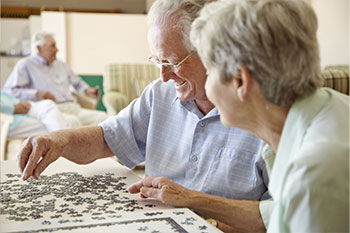 An smiling older man and woman are working together on a jigsaw puzzle.