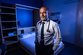 Dr. Rami Khayat stands in a UCI Health sleep lab patient room with a bed in the background.
