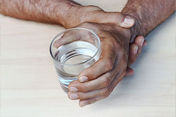A man afflicted with Parkinson's tries to steady his hand that is holding a glass of water.