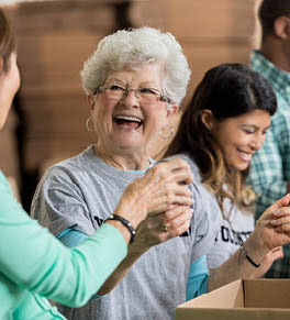 An older, smiling, white woman is volunteering in a food bank.