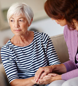 older woman wearing striped shirt with dementia being comforted by another woman with dark hair