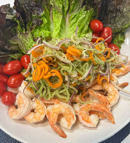 Lemongrass ginger poached shrimp salad is displayed on a white plate on a blue placemat.