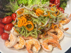 Lemongrass ginger poached shrimp salad is displayed on a white plate with blue placemat.