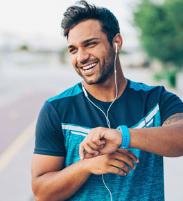 man with tattoos outside exercising and listening to music on earbuds wearing blue shirt and blue wristband; noise pollution is ruining Americans' hearing, says uci health otolaryngologist dr hamid r djalilian