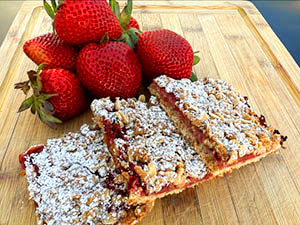 Three slices of Strawberry Oatmeal Streusel Bars with a stack of strawberry behind.
