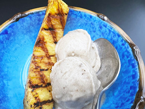 Grilled pineapple spear served with banana ice cream on a blue plate.