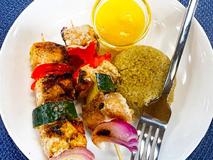 Two chicken skewers with mango sauce and quinoa on the side.
