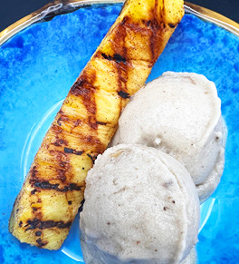 A grilled pineapple spear with two scoops of banana ice cream on a blue plate.