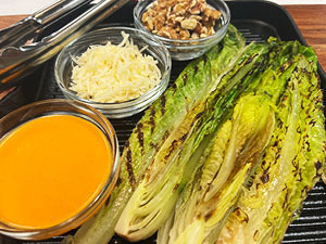 Grilled romaine displayed with bowls of charred red pepper dressing, parmesan cheese and walnuts.
