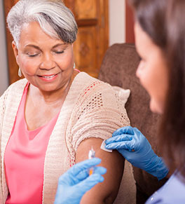A smiling senior Black woman is getting the RSV vaccine from a nurse.
