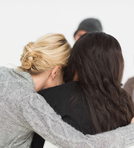 blond woman in gray sweater with her arm around person in black sweater in comfort; injured gun violence survivors are prevalent and some need treatment for years