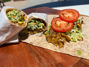 An assembled tofu gyro is displayed with an open whole wheat wrap on a table outside.