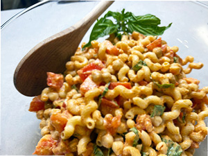 Chickpea pasta is served on a glass plate with a spray of basil and wooden spoon.