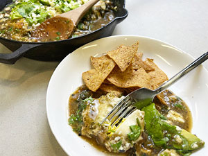 Mexican Green Shaksuka displayed on white plate with corn chips and a cast iron pan to the side.