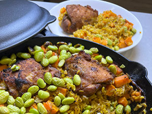 One pan turmeric chicken shown in cast iron skillet and on a plate in the background.