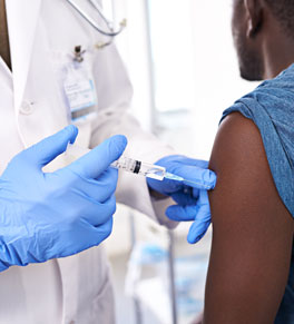 clinician wearing blue latex gloves and white coat gives vaccine to african american person