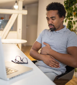 man at desk holding his stomach because of  peptic ulcers pain