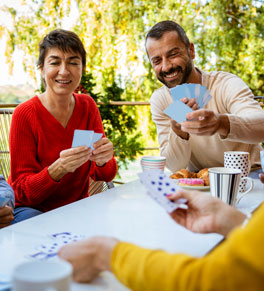 a group of friends playing cards outside at a table covered with a tablecloth; social activity and games can keep your brain healthy says uci health neuropsychologist hayley kristinsson