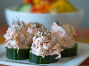The delicious salmon spread is served on cucumber disks with a bowl of veggies in the background.