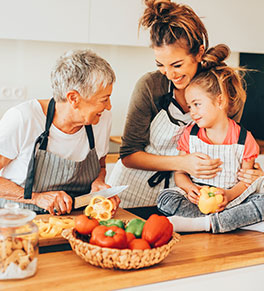 Grandma, mom and granddaughter laughing in the kitchen while chopping bell peppers.