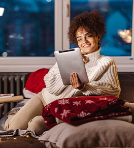 Smiling young woman reading on her tablet in cozy, holiday room.