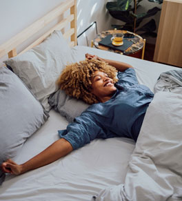 woman waking up in bed in the morning smiling and stretching her arms upward