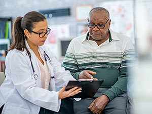 A young woman doctor shows a senior adult male his chart.