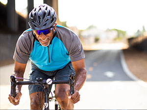 An older Black man wearing a helmet is happily cycling on a road.