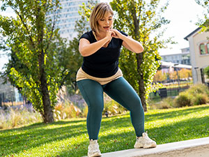 An overweight woman is doing squats outside.