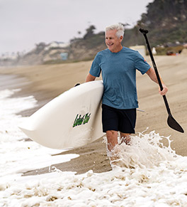 Steve Mellem carries his paddleboard into the waves with gusto after defeating prostate cancer.