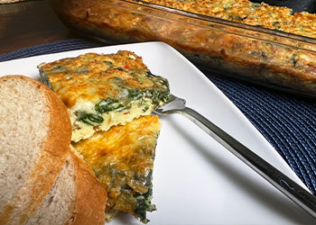 Two slices of egg and vegetable casserole is displayed on a white plate with the casserole dish in the background.